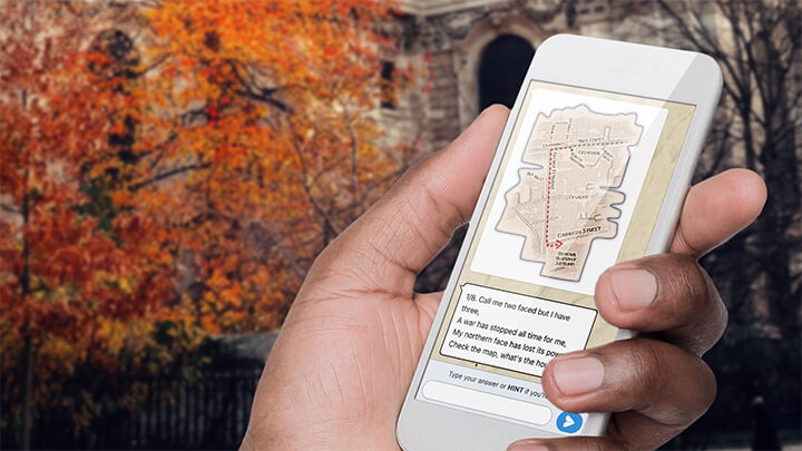 A hand holding a phone playing Treasure Hunt Oxford with a tree with orange leaves behind.